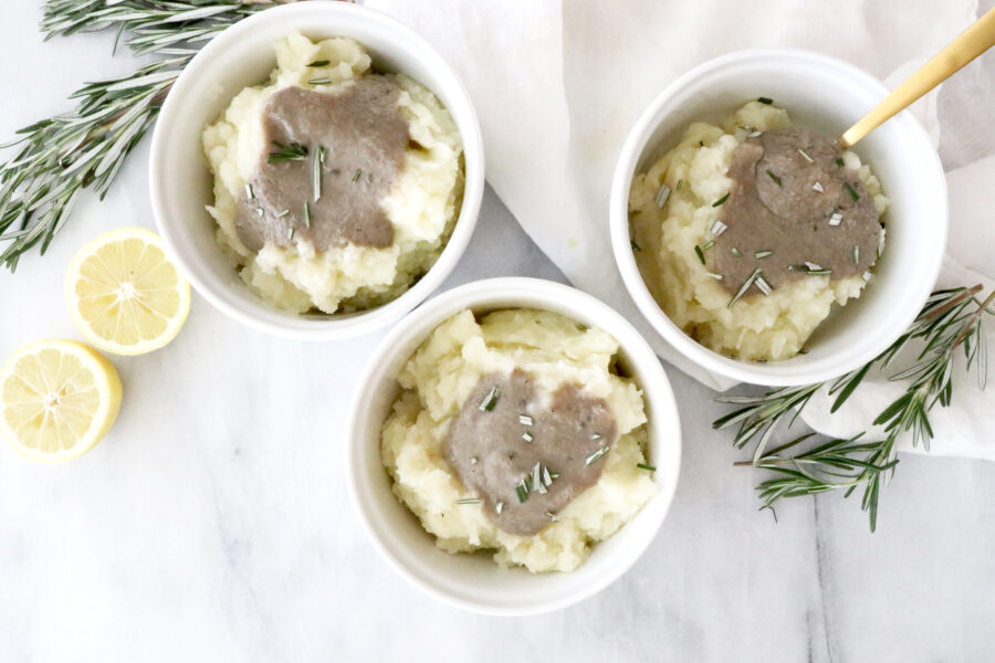 Three white bowls filled with mashed potatoes and gravy. Lemons and rosemary on the sides.
