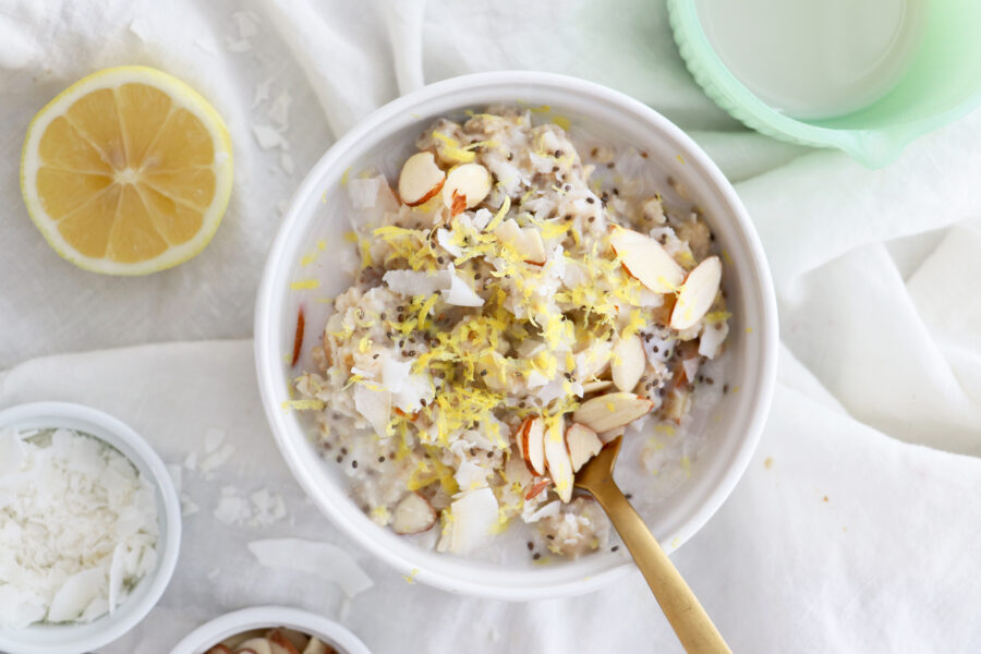 White bowl with oatmeal topped with sliced almonds and gold spoon on side. 