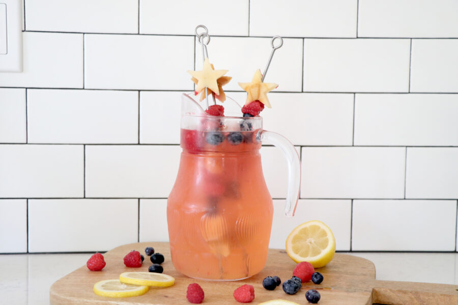 Lemon, raspberry and blueberry infused lemonade in clear pitcher.