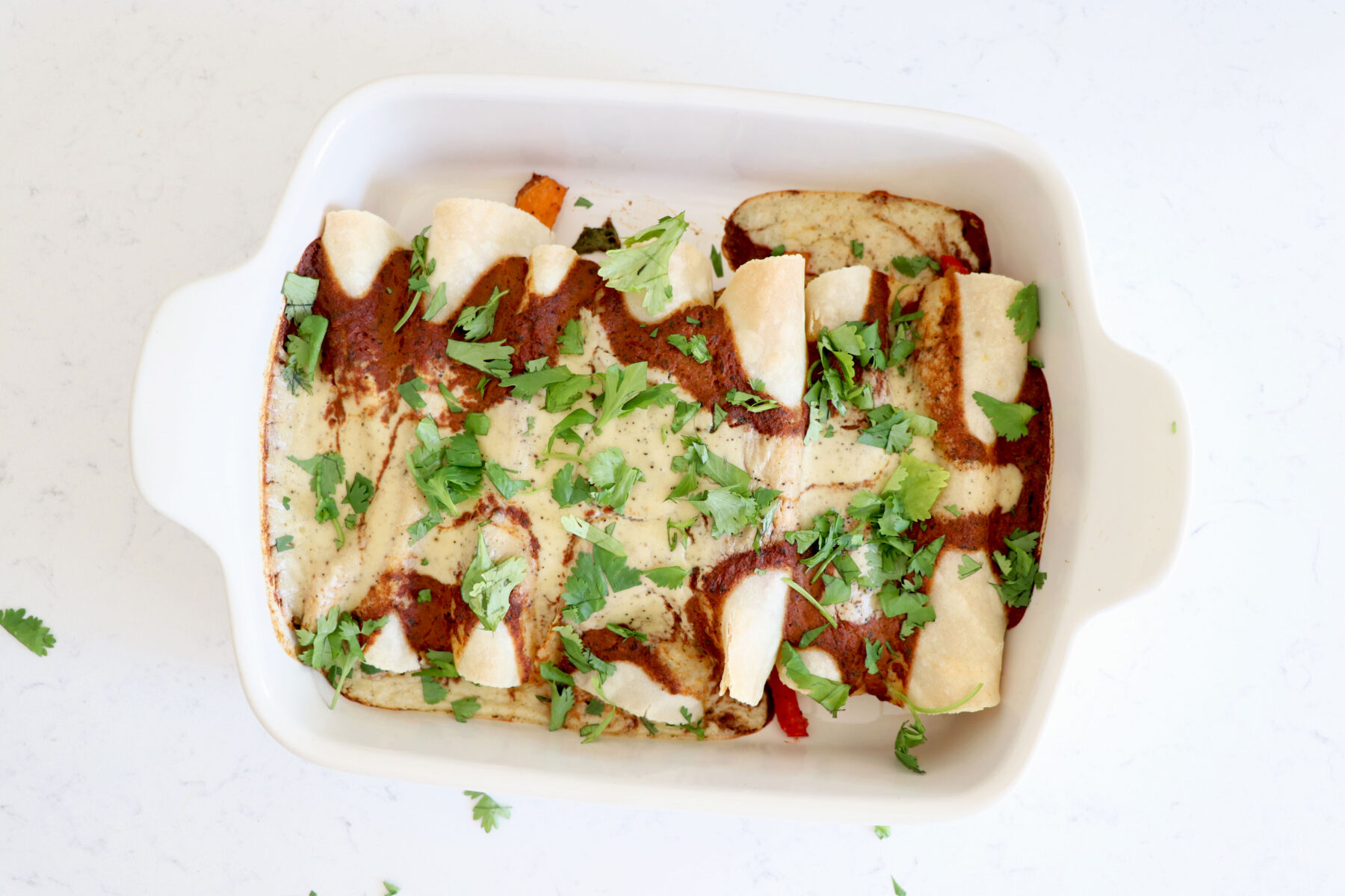 Baking dish with enchiladas covered with a red mole sauce and cashew cream sauce.